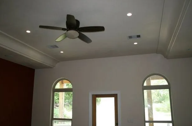 Ceiling fan and recessed lights in a room with arched windows and a wooden door.