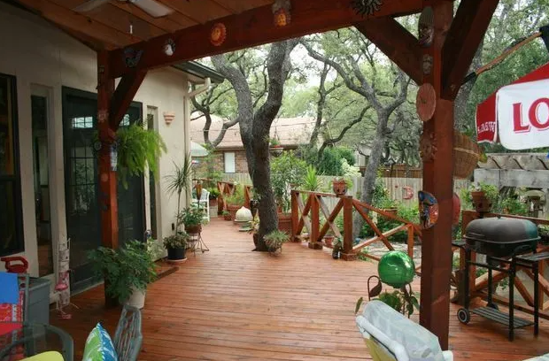 Wooden deck and covered porch with a grill, plants, and trees in the background.