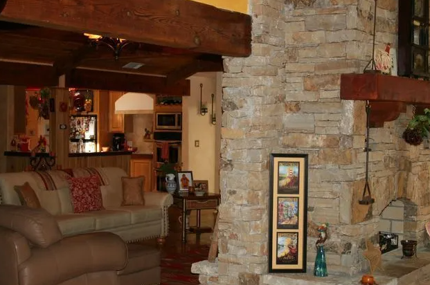 Living room with stone wall, exposed wooden beams, and view into kitchen.