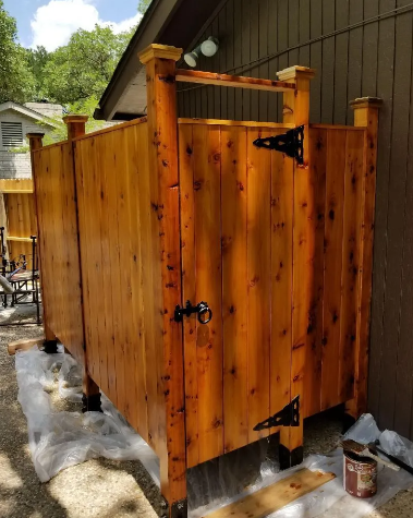 Outdoor wooden shower stall with door, black hardware, and clear coating.
