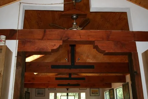 Rustic wooden doorway with decorative beam and ceiling fan. Interior view with a glimpse of another room.