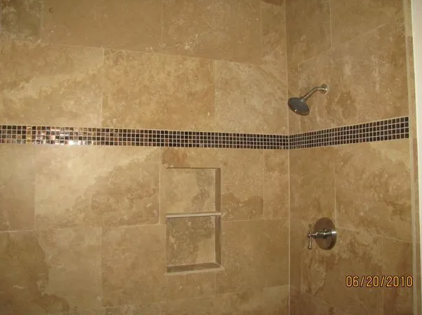 Beige tiled shower with dark mosaic tile accent, built-in shelf, and chrome fixtures.