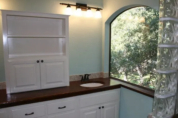 Bathroom with white cabinets, dark countertop, and arched window with a view.