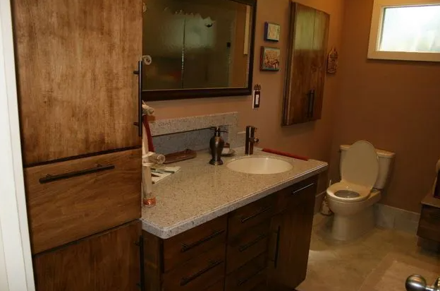 Bathroom with wooden cabinets, a sink, toilet, mirror, and a small window.