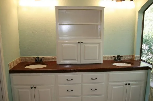 Bathroom with white cabinets, dark countertop, dual sinks, and a centered cabinet.