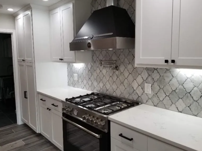 White kitchen with white cabinets, stainless steel range and range hood, marble tile backsplash.