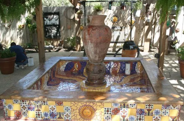 Fountain with a large ceramic pot centerpiece, mosaic tile details, in a courtyard setting.