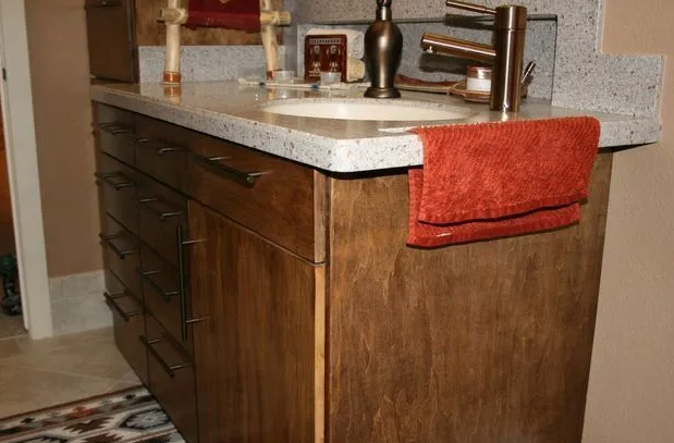 Bathroom vanity with brown cabinets, gray countertop, and orange towel.