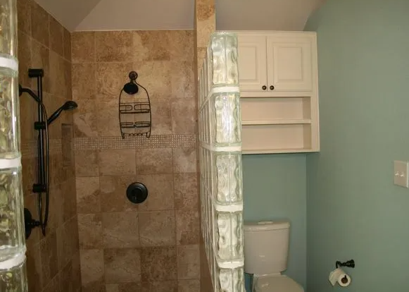 Bathroom with a tiled shower, glass block wall, and toilet near a cabinet on a blue wall.