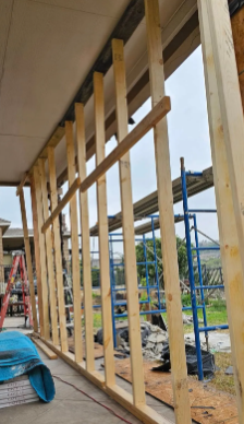 Wooden framework for a wall under construction, outdoors. Lumber pieces are vertical and horizontal.