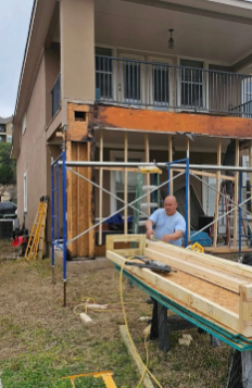 Construction worker on scaffolding, repairing a building's exterior.  Exterior wall is open; lumber and tools are visible.