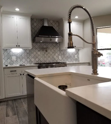 Modern kitchen with white cabinets, farmhouse sink, stainless steel faucet, and patterned backsplash.