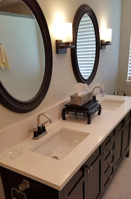 Bathroom with dark cabinets, white countertop, two oval mirrors, and sconce lighting.