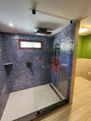 Shower with blue mosaic tile walls and glass door, next to a wood-toned wall and green wall.