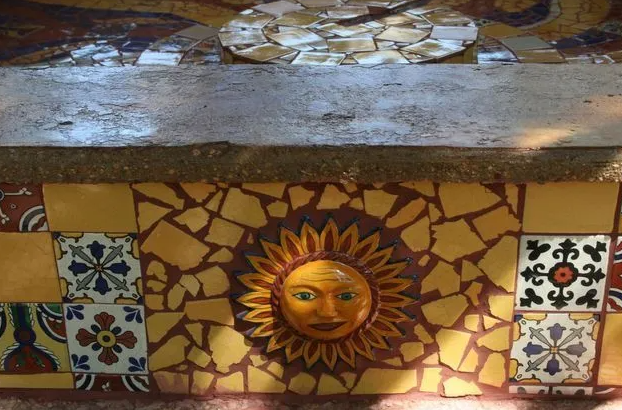 Mosaic sunburst with a face, set into yellow tile and stone.