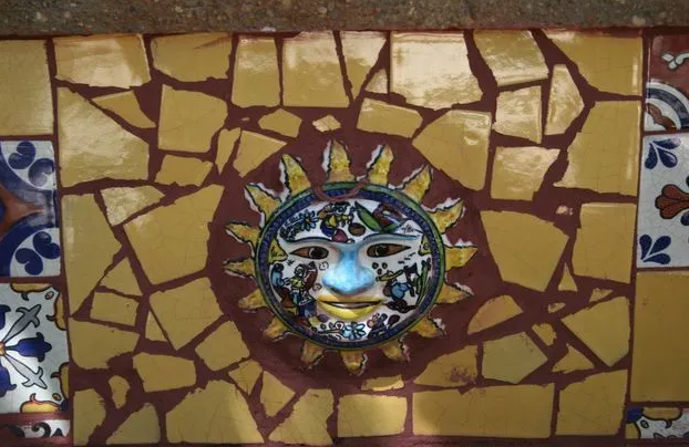 Decorative sun face mosaic surrounded by yellow and brown tiles.