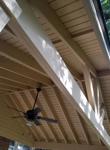 Beige wood ceiling with exposed beams, a ceiling fan, and a gutter, viewed from below.