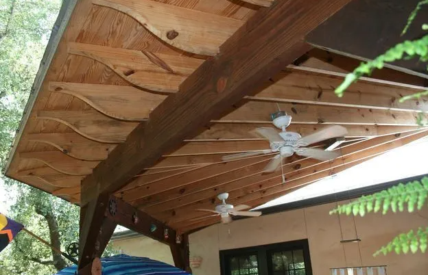 Wooden patio roof with decorative wavy ceiling, support beams, and ceiling fans.
