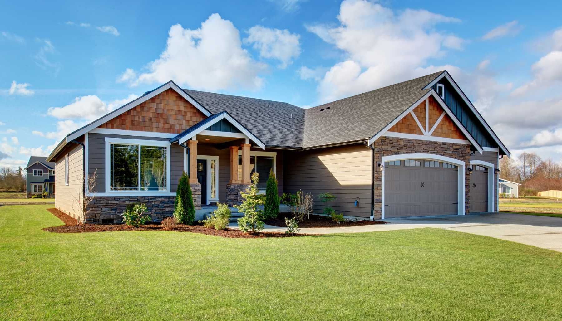 Gray, single-story house with a lawn, blue sky, and a two-car garage. Brown wood accents and landscaping.