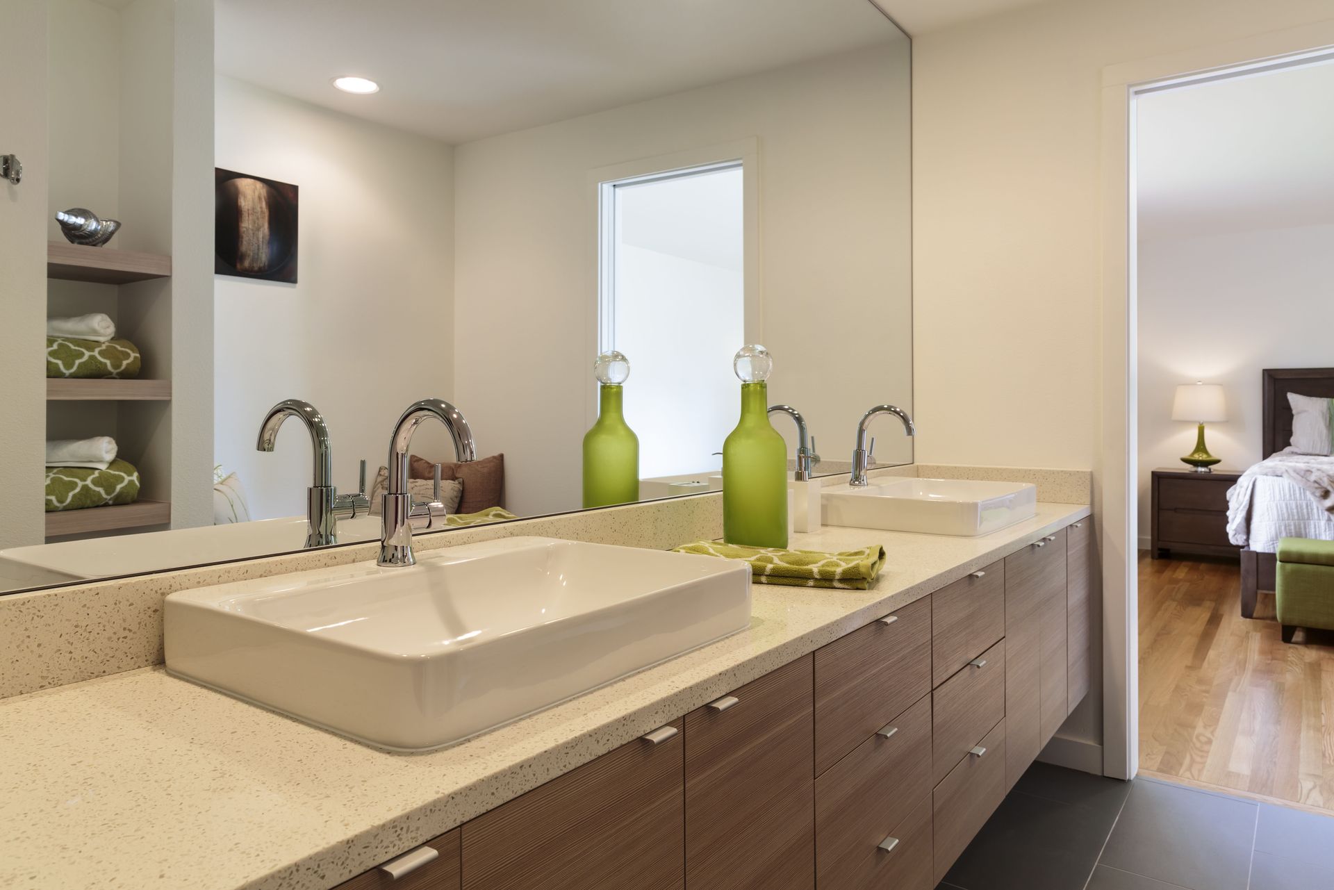 Bathroom with double sinks, large mirror, wooden cabinets, and an open doorway to a bedroom.