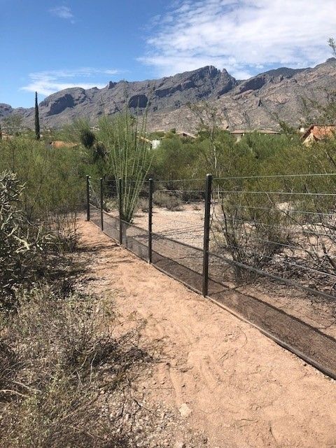 a fence surrounds a dirt path in the desert with mountains in the background