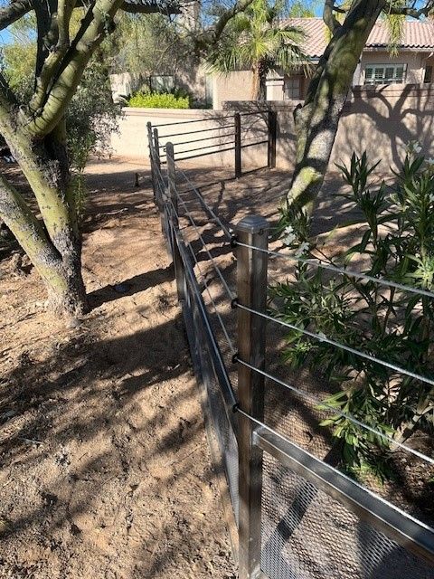 a metal fence is surrounded by trees and dirt in a yard