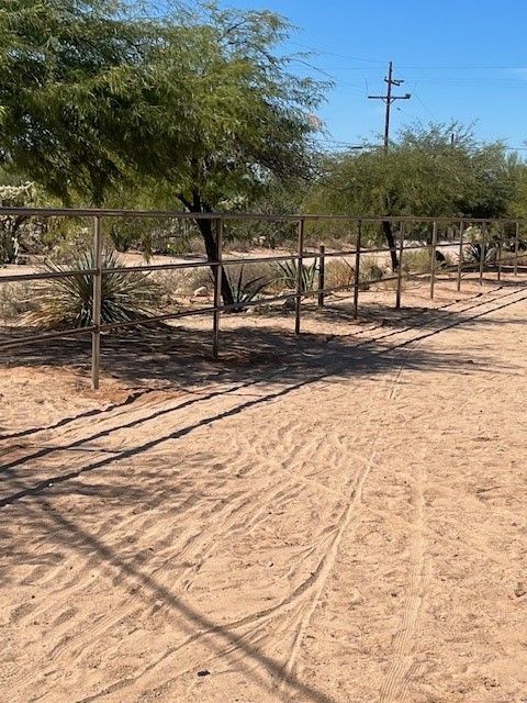 a fence in the middle of a dirt field with trees in the background