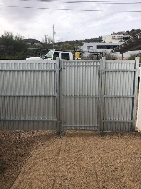 a corrugated fence with a gate and a truck in the background
