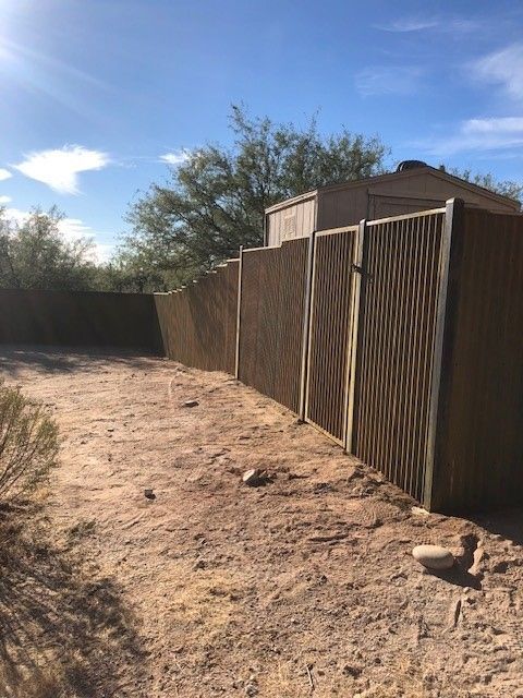 a corrugated fence is in the middle of a dirt field