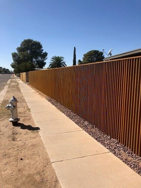 a fire hydrant is on the sidewalk next to a corrugated fence