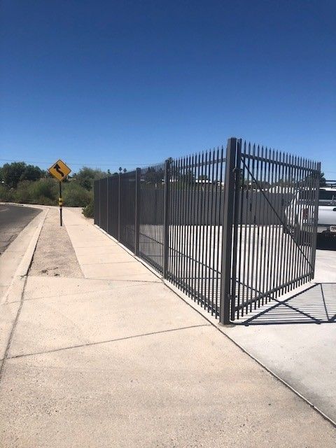 a metal fence along a sidewalk with a yellow sign that says