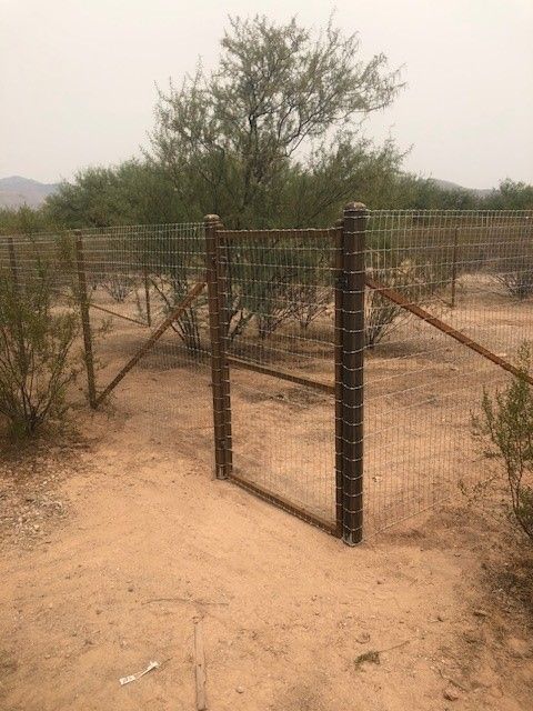 a fence with a gate in the middle of a dirt field