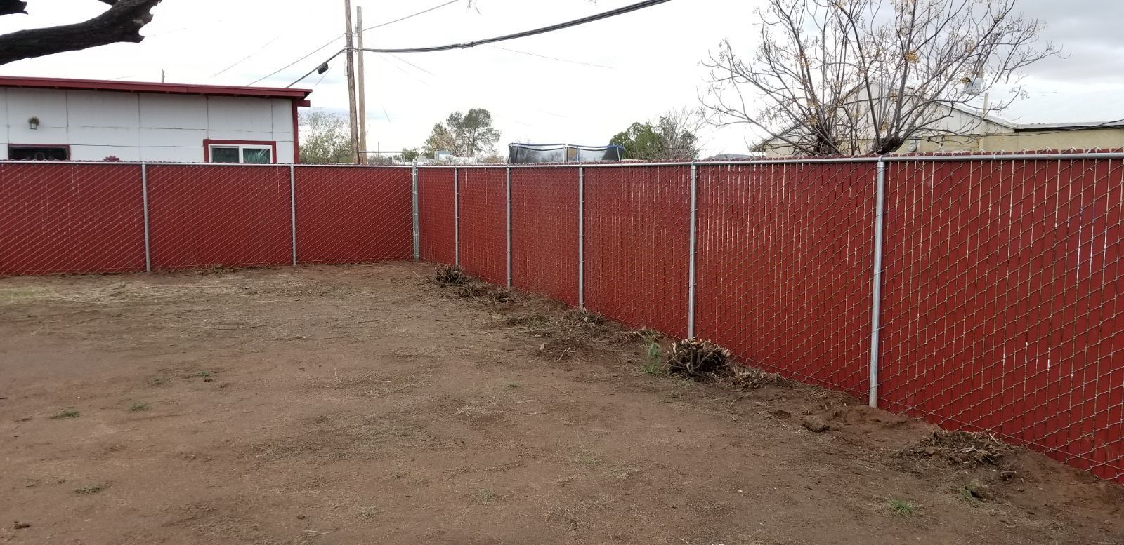 a red chain link fence surrounds a dirt yard