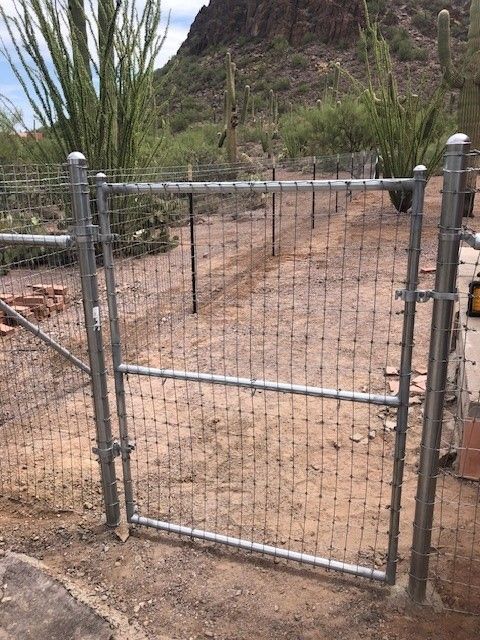 a metal fence with a gate in the middle of a dirt field