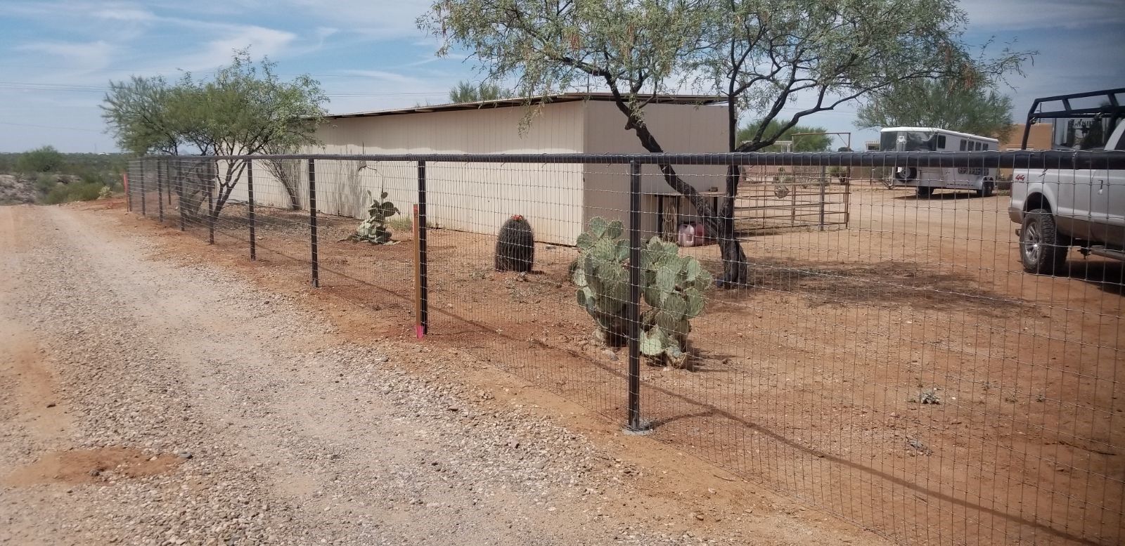 a fence surrounds a dirt road with a truck parked in the background
