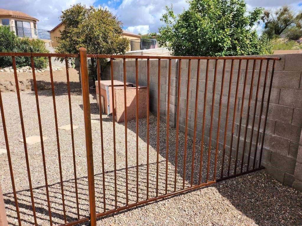 a rusty metal fence is surrounded by gravel and a brick wall