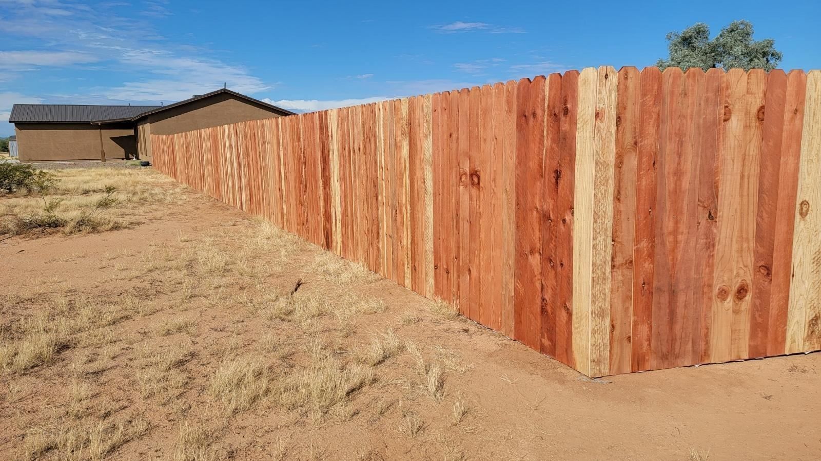 a wooden fence is sitting in the middle of a dirt field in front of a house