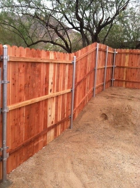 a wooden fence surrounds a dirt area with trees in the background