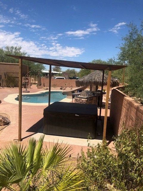 a hot tub is under a pergola next to a swimming pool