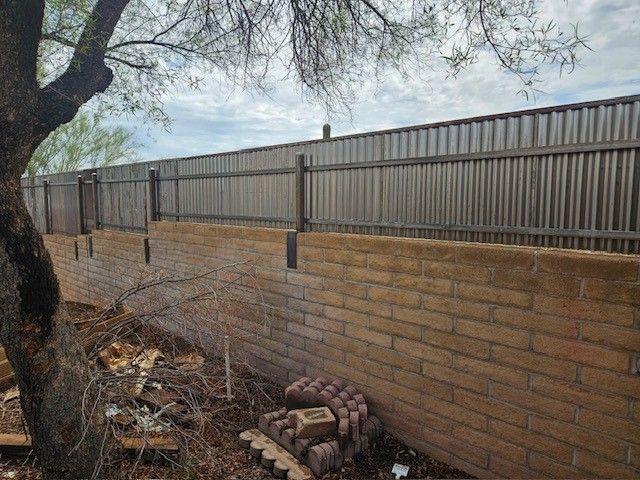 a brick wall with a metal fence and a tree in the background