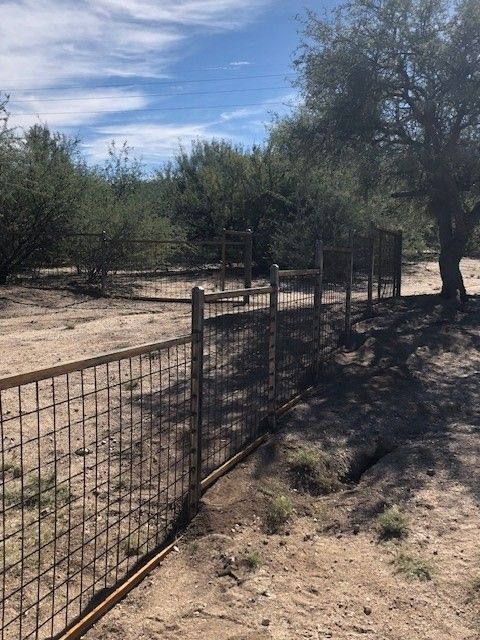 a fence surrounds a dirt field with trees in the background