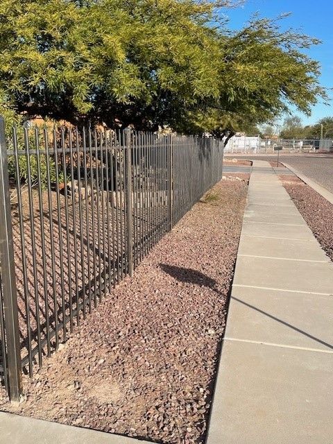 a metal fence along a sidewalk with trees in the background