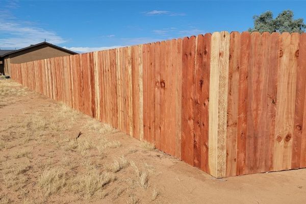 A wooden fence is sitting on top of a dirt field next to a house.