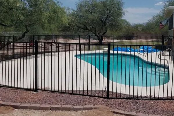A black metal fence surrounds a large swimming pool.