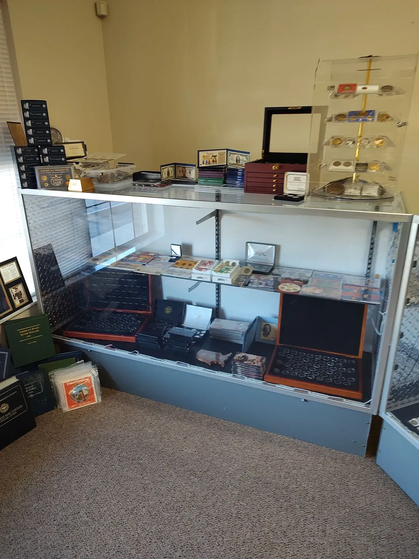 A glass display case in a room filled with items like coins, jewelry, and other collectibles.