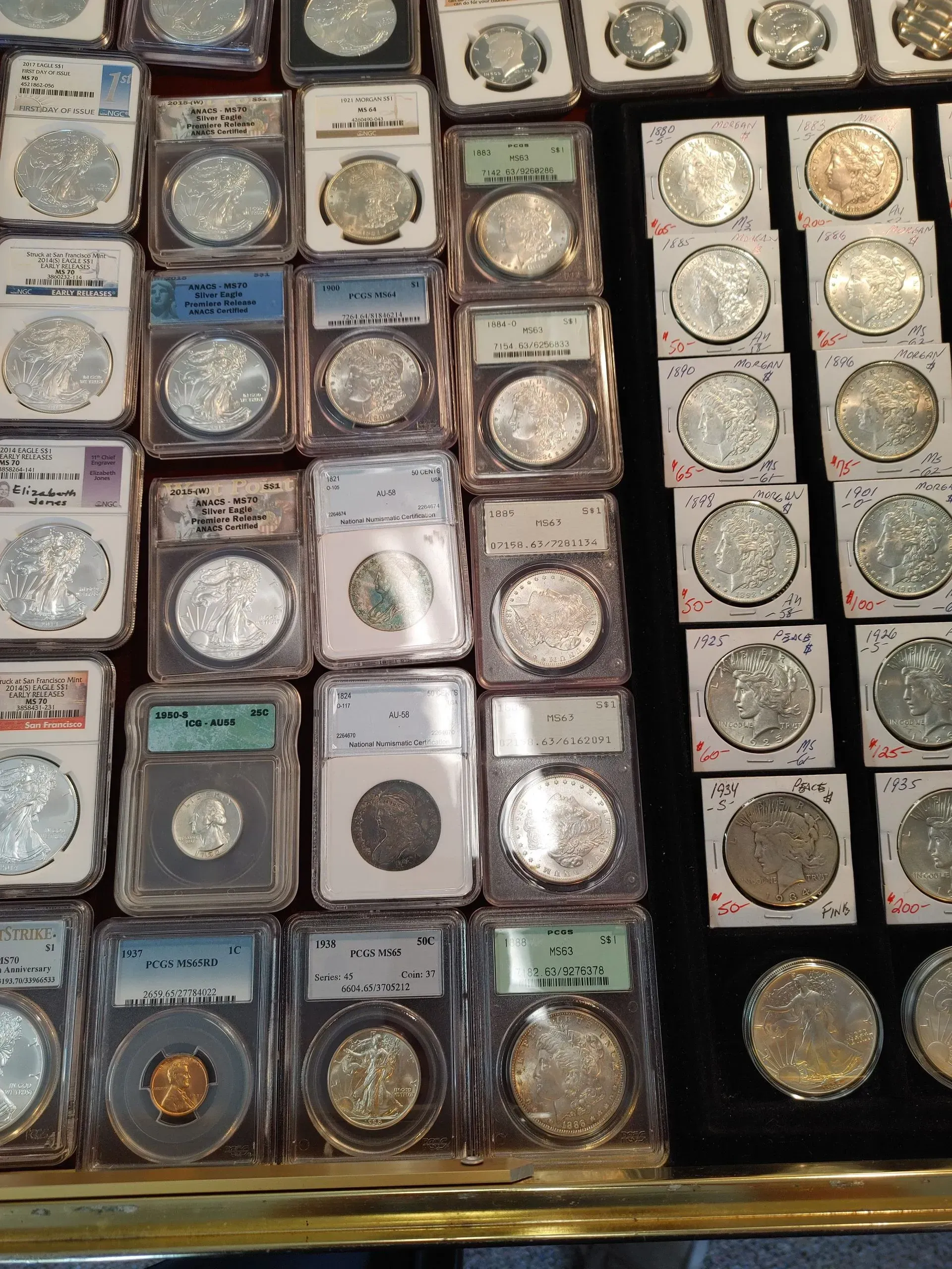 Coins in plastic cases, displayed in rows on a dark surface. Some cases are labeled with grades.