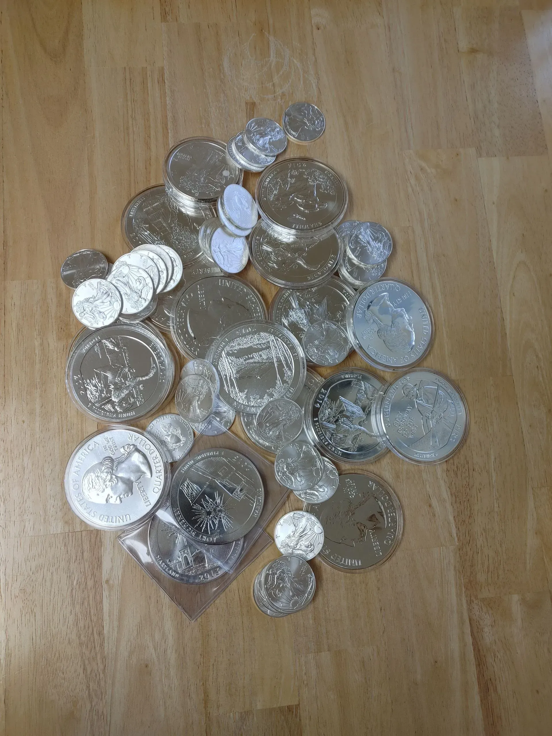 Pile of silver coins on a wooden surface. Some coins are in a plastic bag.