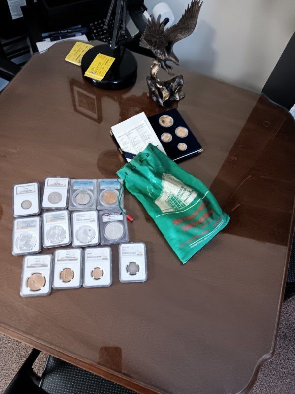 Glassed table with organized coin sets, a green pouch, and a decorative eagle statue on a black stand.