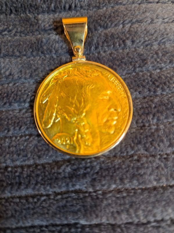 Gold circular pendant with a raised profile design on a dark textured fabric background