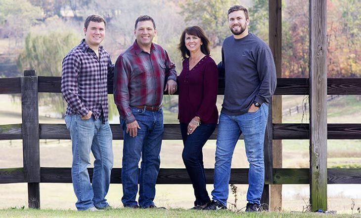 A family is posing for a picture in front of a wooden fence.